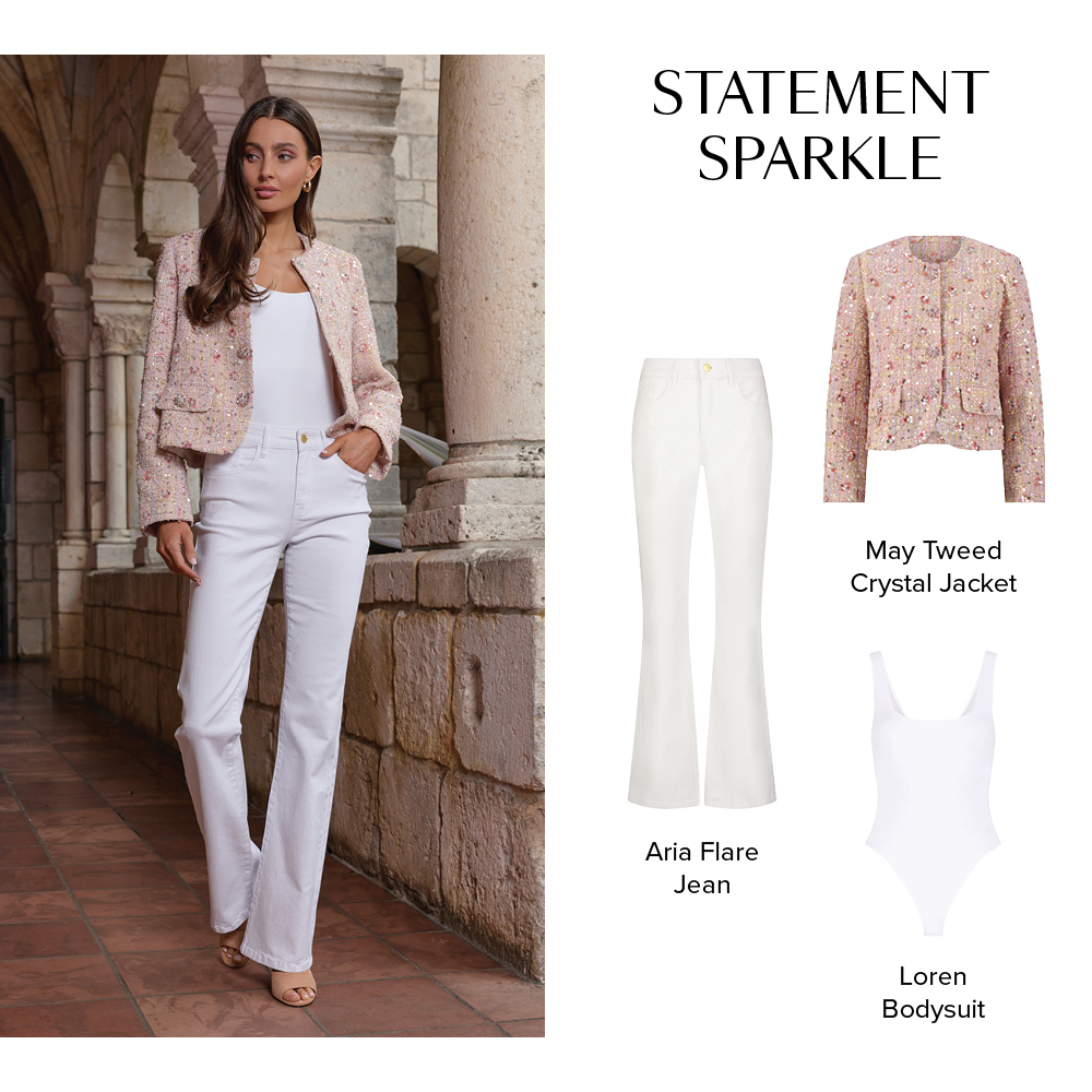 Statement Sparkle. A model is posed in a stone corridor wearing the Pink Multi May Tweed Crystal Jacket, White Loren Bodysuit, and White Aria Flare Jean.
