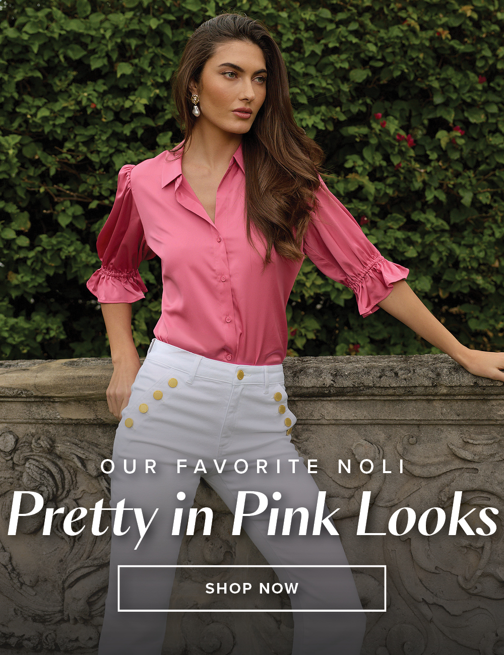 Our Favorite Noli Pretty in Pink Looks. Shop Now. A model is posed in front of a stone ledge with a lush green hedge behind her  wearing the Petal Pink Cindy Ruffle Sleeve Blouse