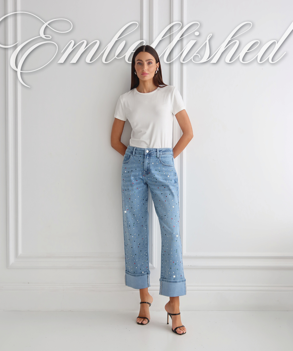 Embellished. An image of a model standing posed on a minimal white wall wearing the embellished Confetti Ren Cropped Cuff Jean. 