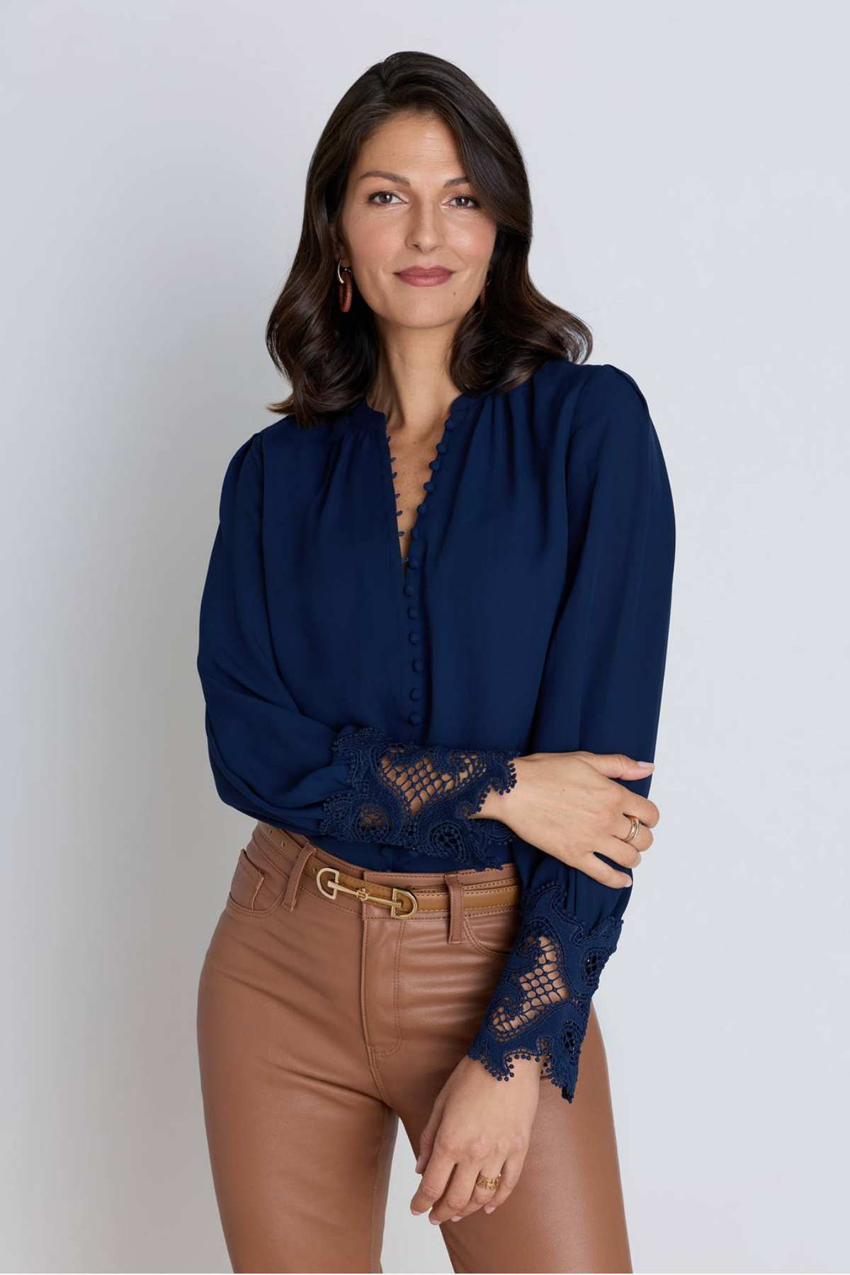Woman in a navy crepe blouse with covered buttons and lace cuffs, tucked into mocha coated jeans with a thin gold belt.Woman in a navy crepe blouse with covered buttons and lace cuffs, tucked into mocha coated jeans with a thin gold belt.