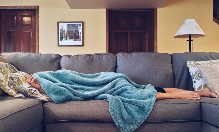 Someone resting on a couch under a soft blue blanket