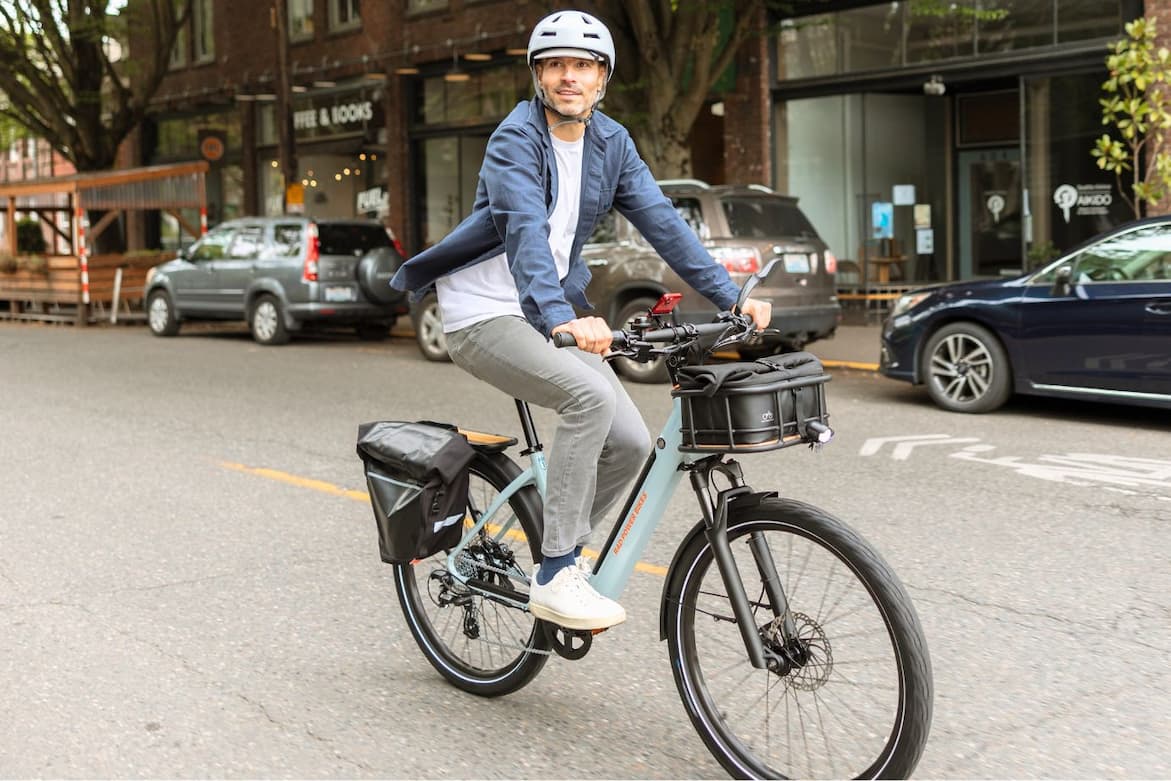 A man rides a RadKick with a basket and bag on it down a city street.
