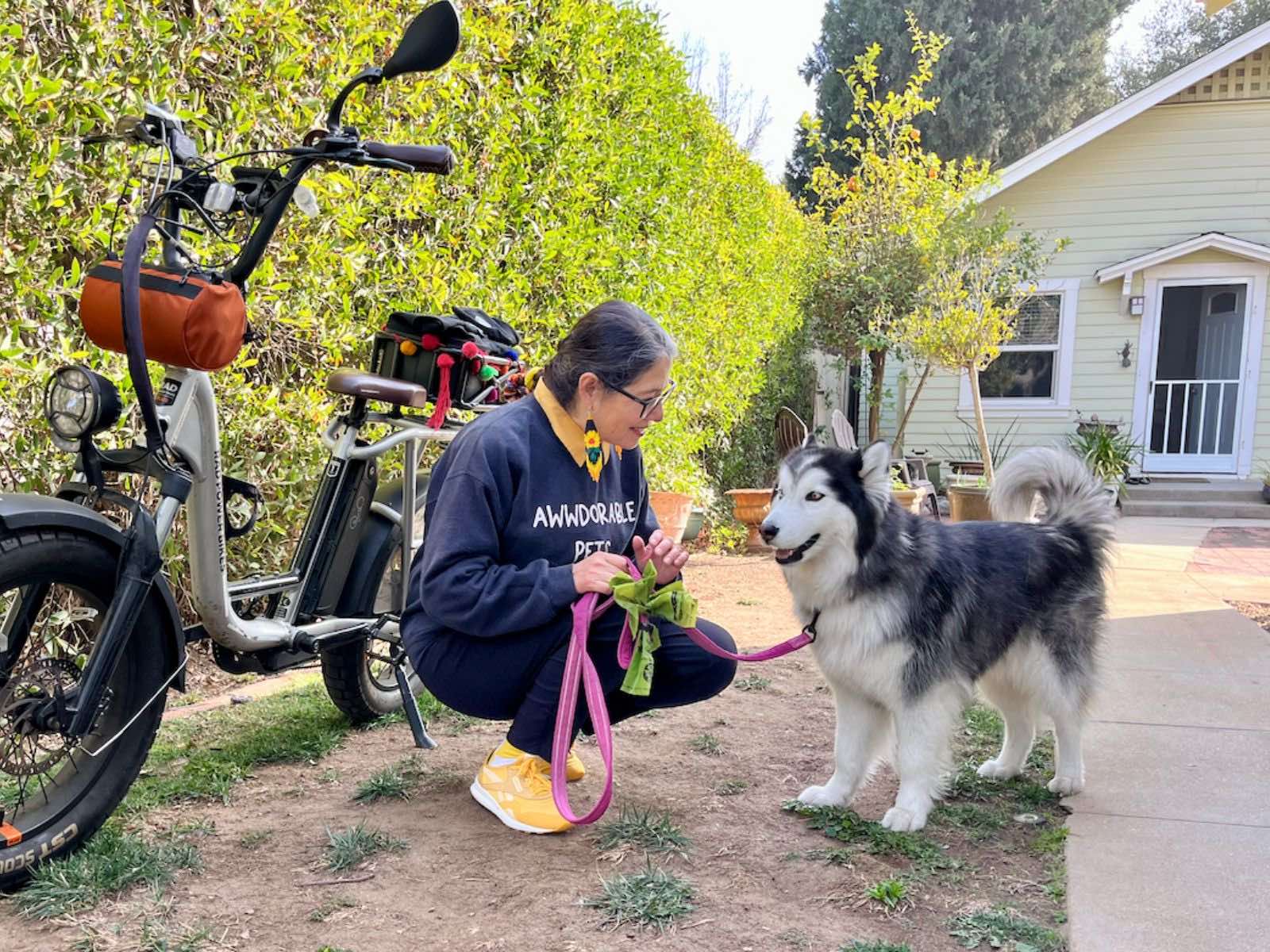 A woman tends to a black and white dog alongside a silver RadRunner in a sunny backyard 