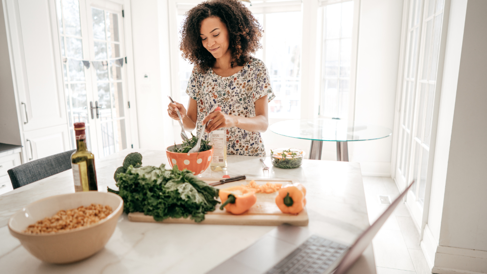 woman making salad in kitchen with greens, peppers & healthy ingredients