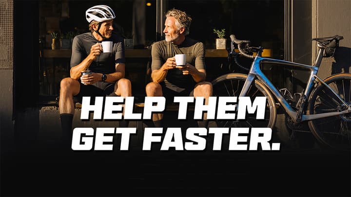Two women in cycling gear drink coffee next to a purple bike with text "HELP THEM GET FASTER."