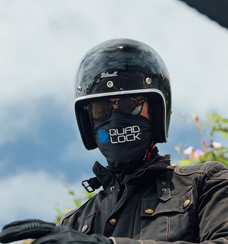 A photo of a mortorcyclist is wearing the Quad Lock Neck Gaiter under their motorcycle helmet and black sunglasses