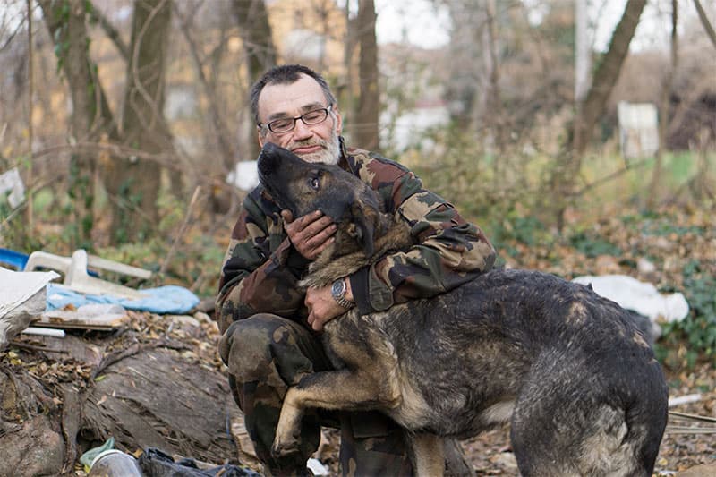 Man sitting down petting a dog.