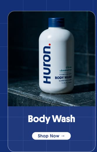 Huron Body Wash bottle on wet stone shower ledge with "Shop Now" button.