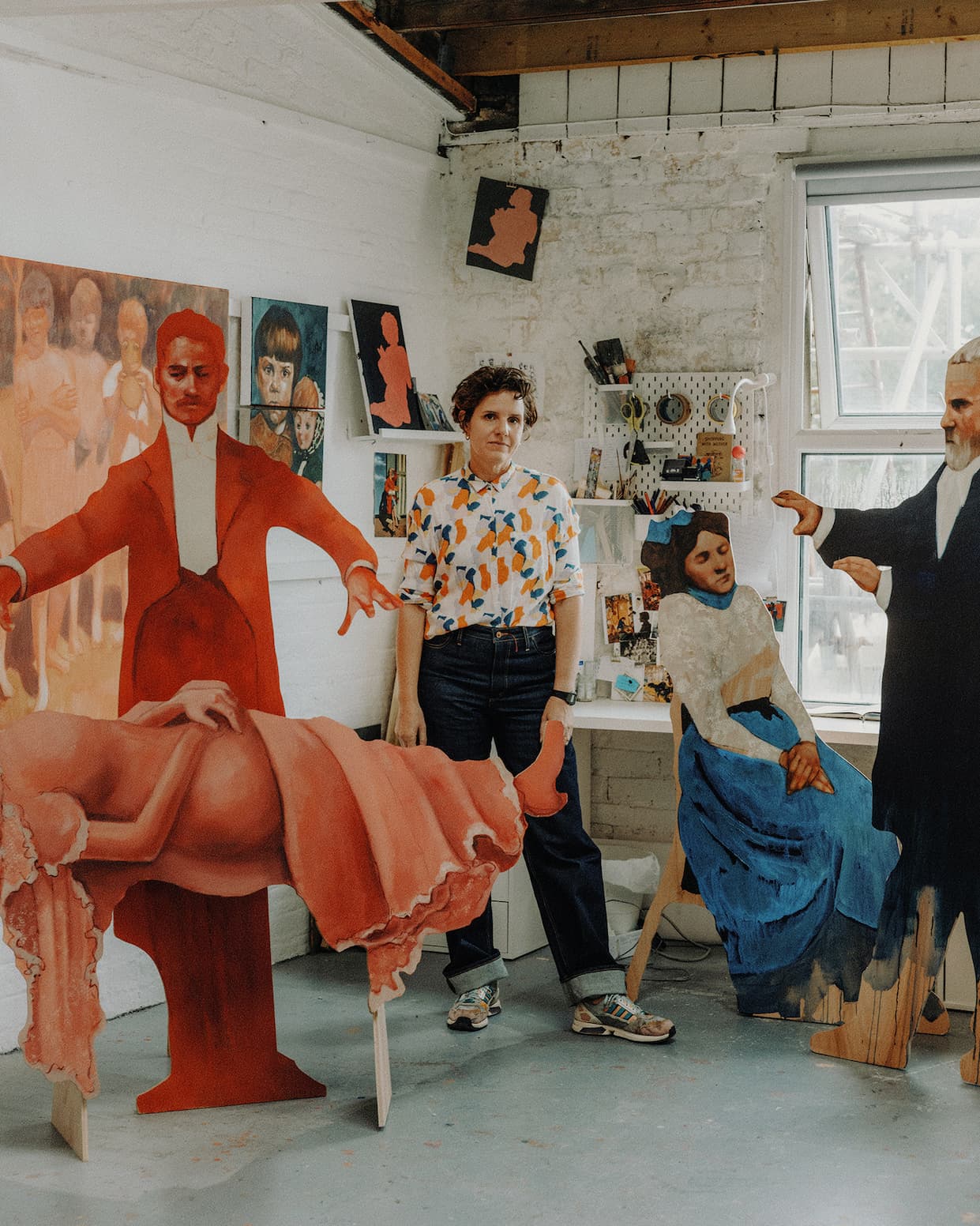 Amy Dury stands in her studio wearing jeans and colourful shirt.