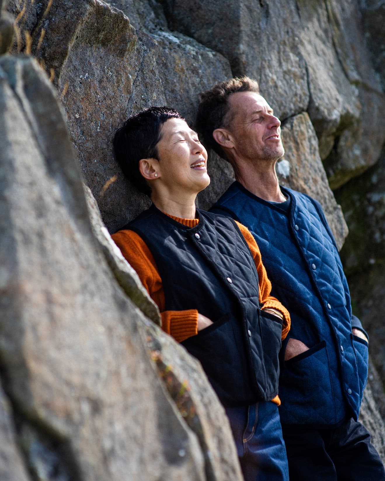 a man and a woman leaning on a rock smiling.