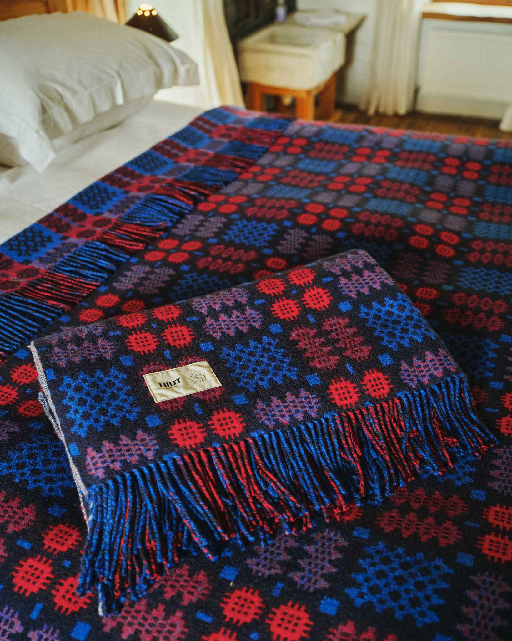 Photo of red and navy blue Welsh blanket on bed with another blanket folded neatly on top.