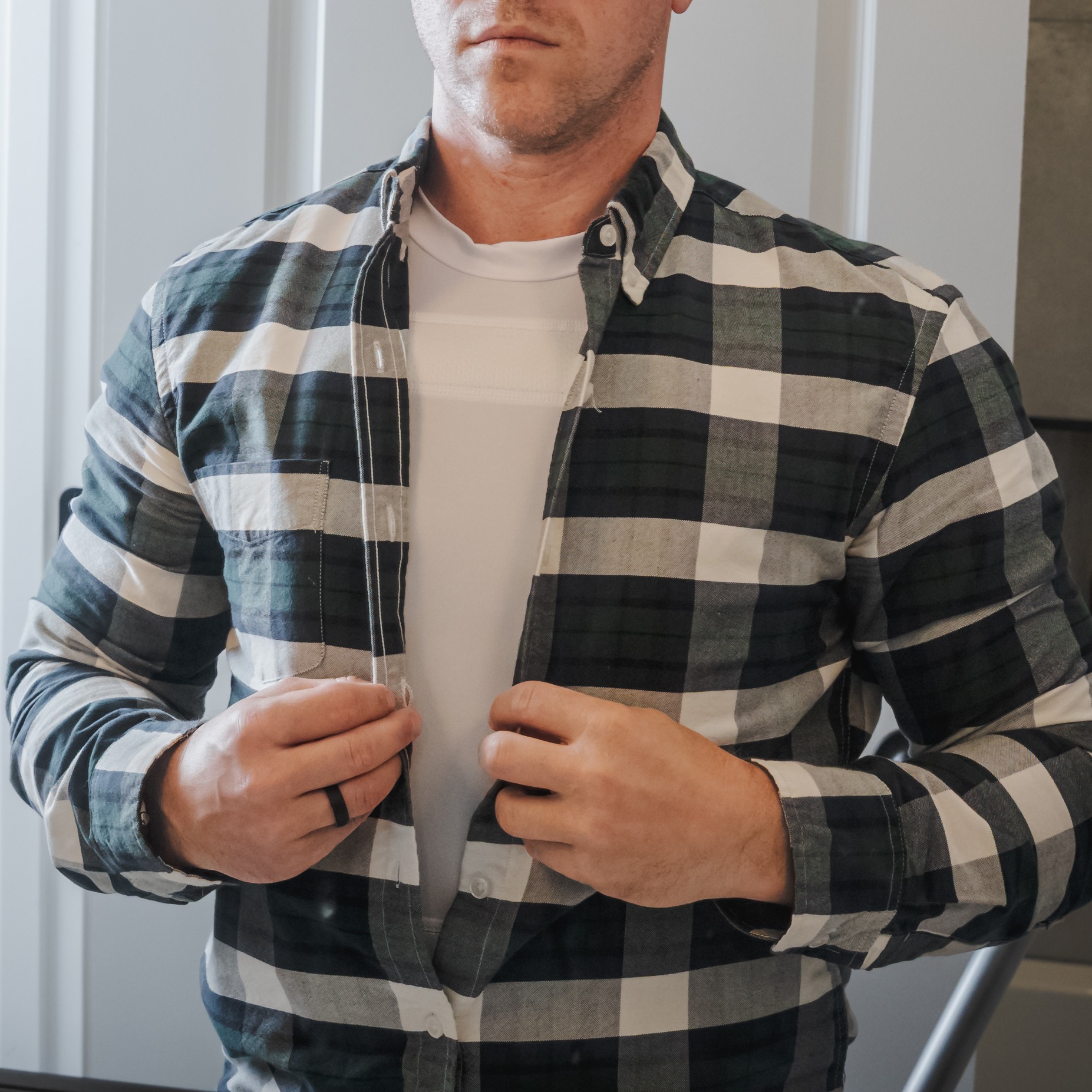 mean buttoning plaid shirt over white armor t-shirt