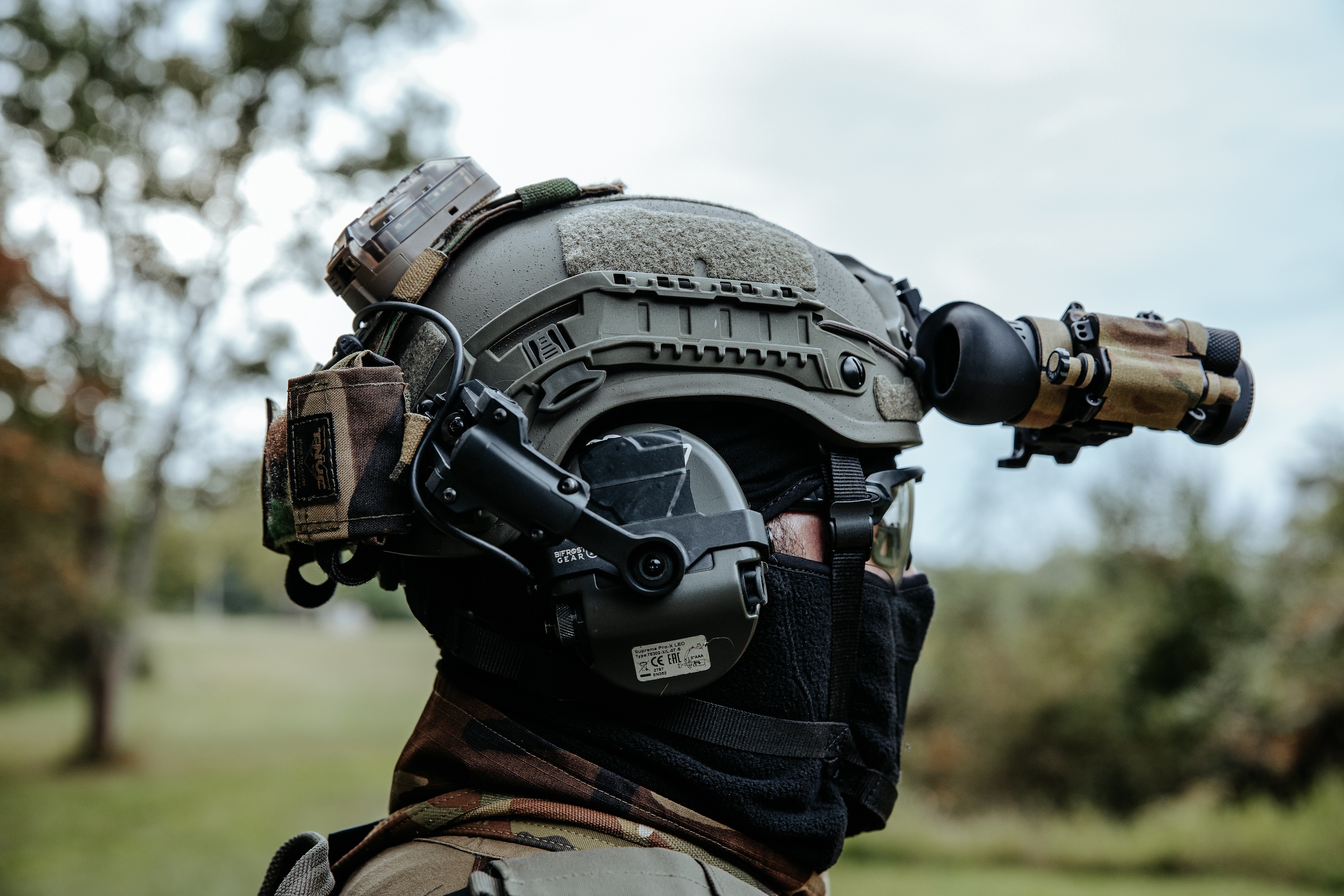 man wearing green ballistic helmet with nvg, ear pro, and other gear