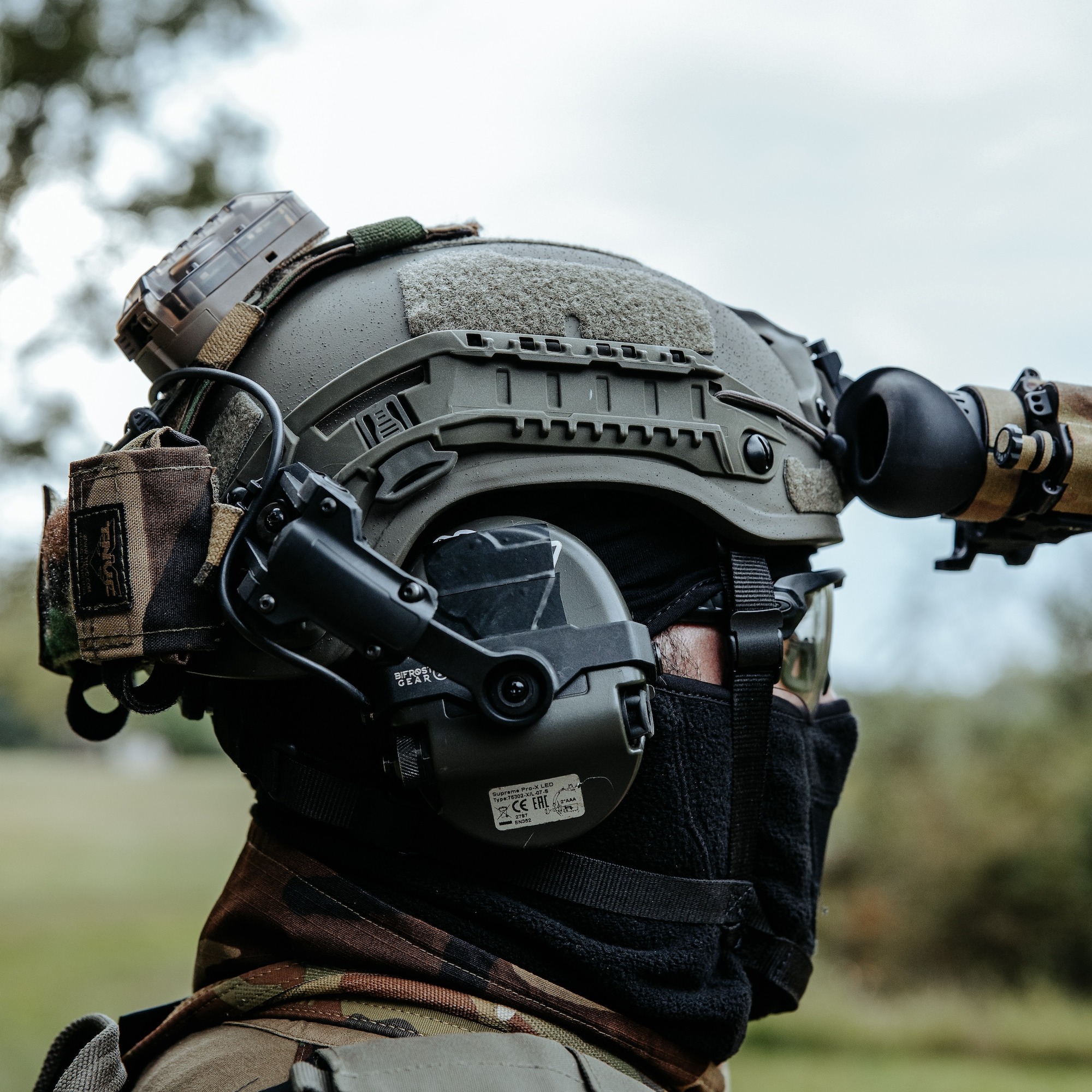 man wearing green ballistic helmet with nvg, ear pro, and other gear