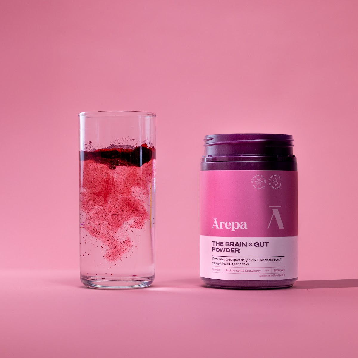 Ārepa Brain x Gut Powder dissolving in a glass of water next to the tub