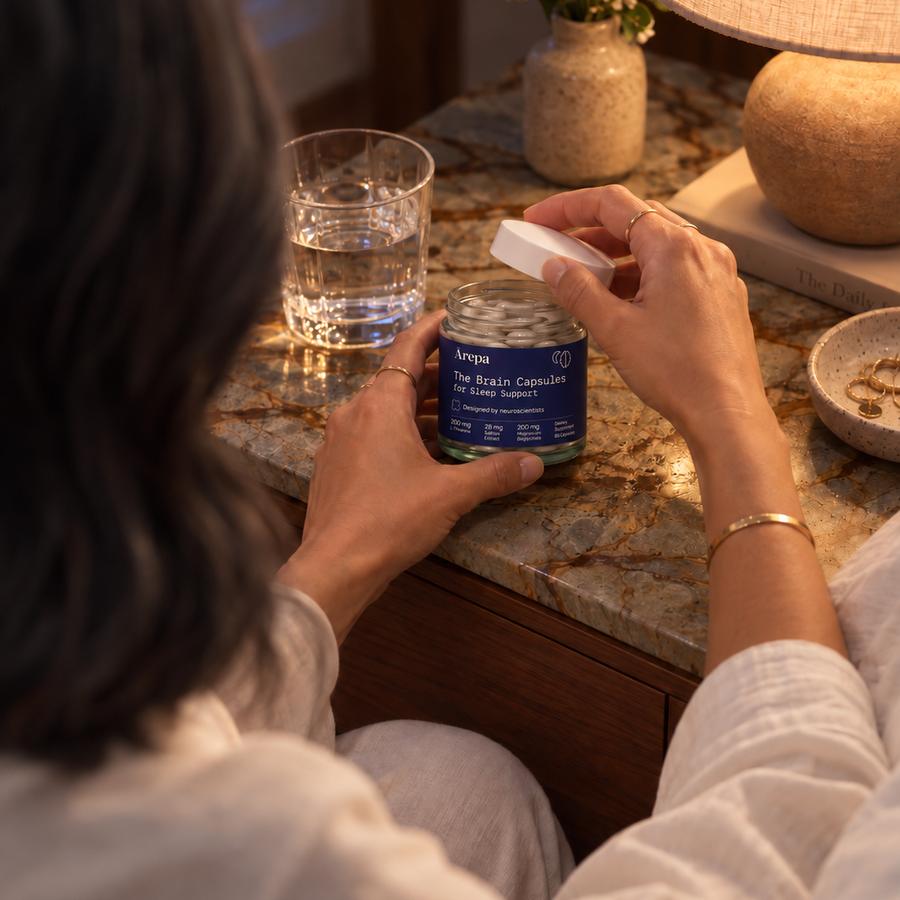 Opening a jar of The Brain Capsules for Sleep Support on a bedside table