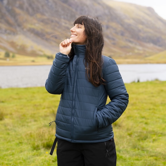 Smiling woman zipping up a mid-layer jacket in the outdoors