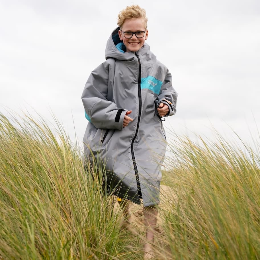 Smiling young boy running through the sand dunes while wearing a Dryrobe®
