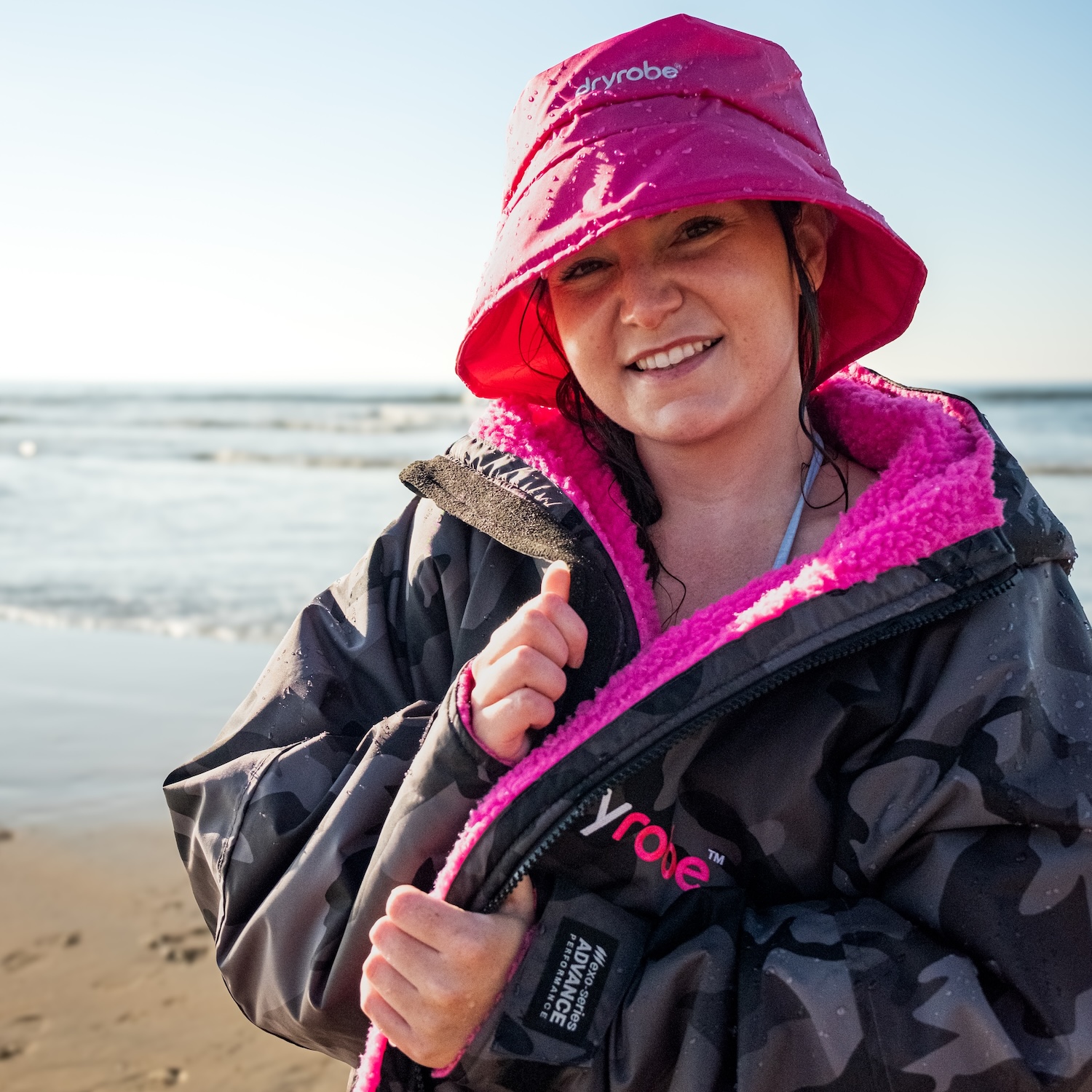 Smiling female wearing a bucket hat and dryrobe® Advance on the beach
