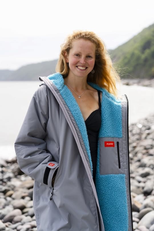 Smiling woman wearing a Dryrobe® with a coastal scene in the background
