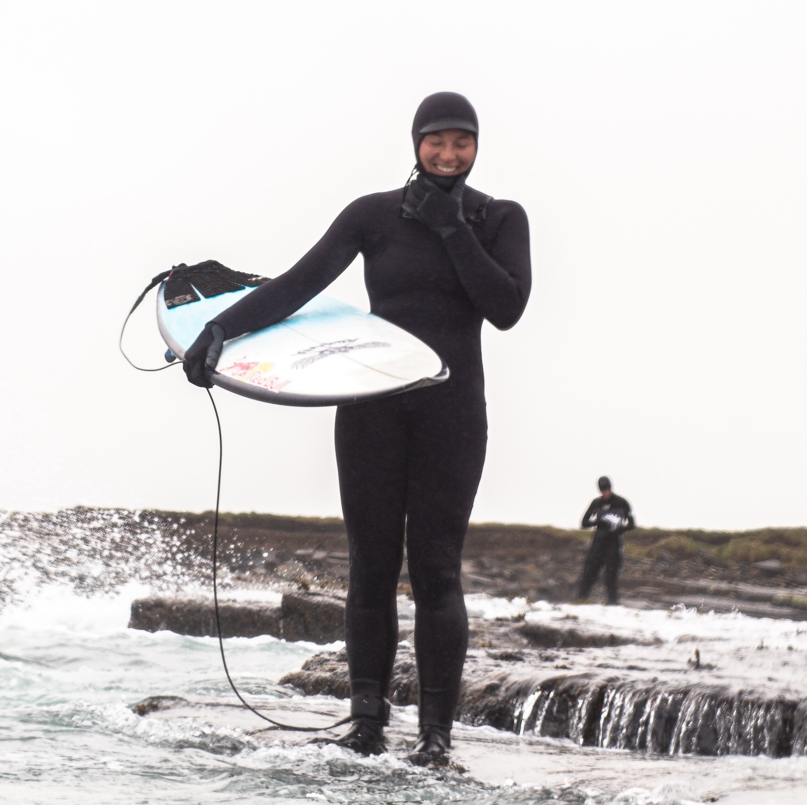 Big wave surfer Izzie Gomez in her wetsuit, carrying a surfboard out of the sea