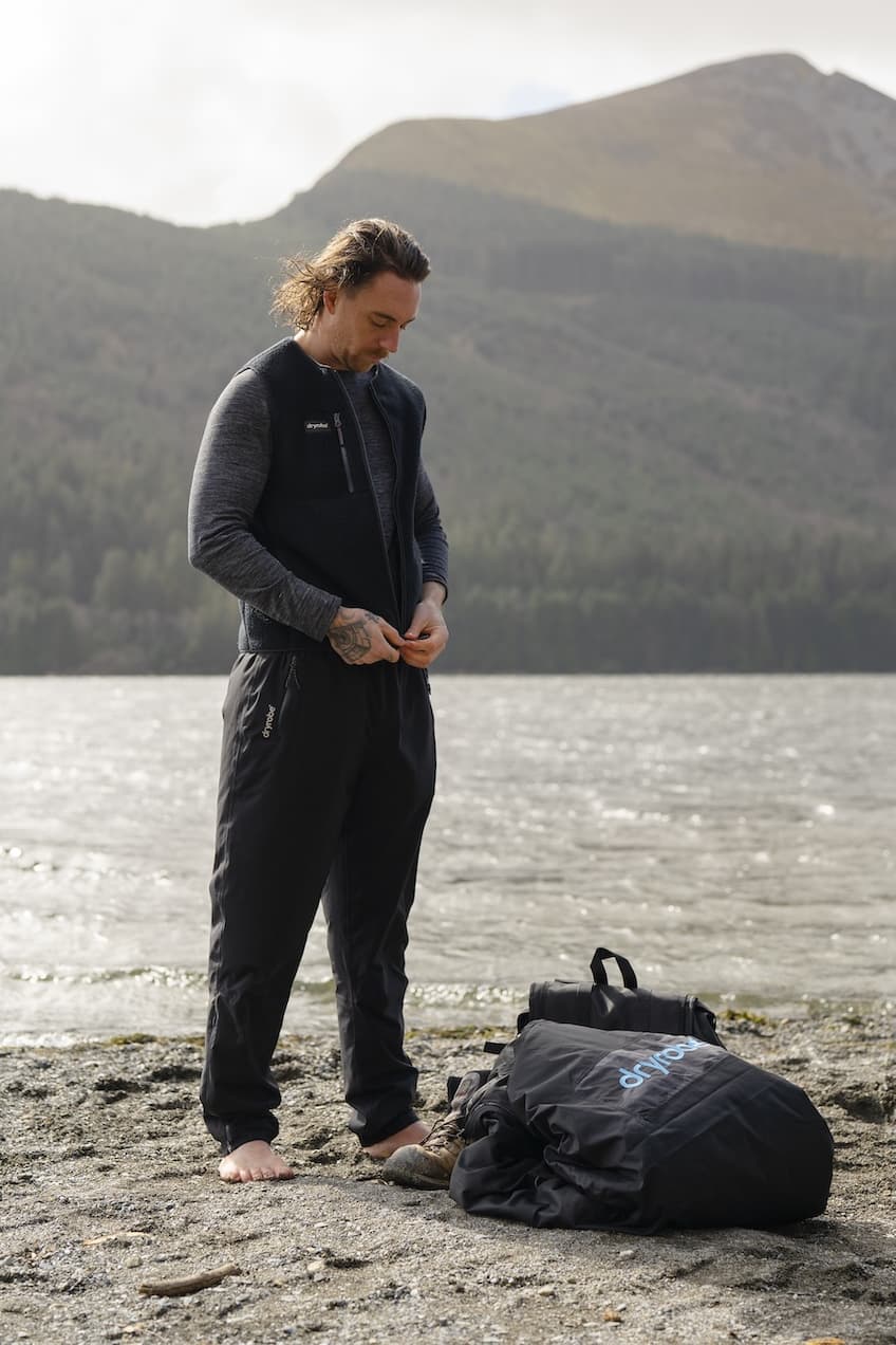 Man wearing thermal trousers beside a lake with mountains in the background