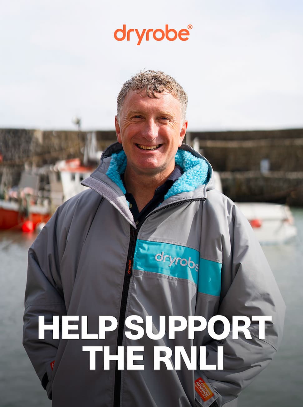 Smiling man wearing a Dryrobe® with the harbour and boats in the background