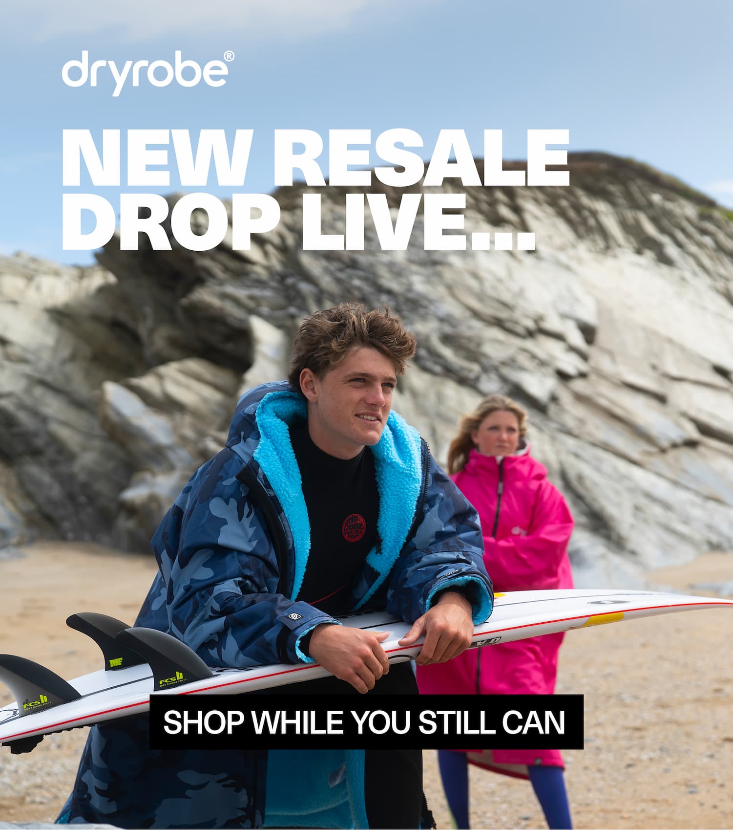 Man and woman on the beach with a surfboard wearing Dryrobe®