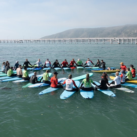 Group of surfers sitting on their boards in the ocean while holding hands