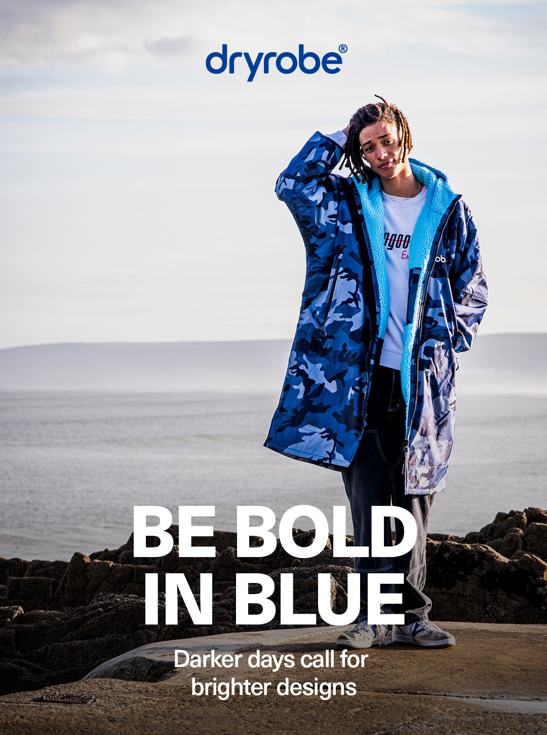 Man wearing a blue camo dryrobe® with the coastline in the backdrop