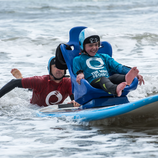 Young disabled surfer in the water with a surfing volunteer