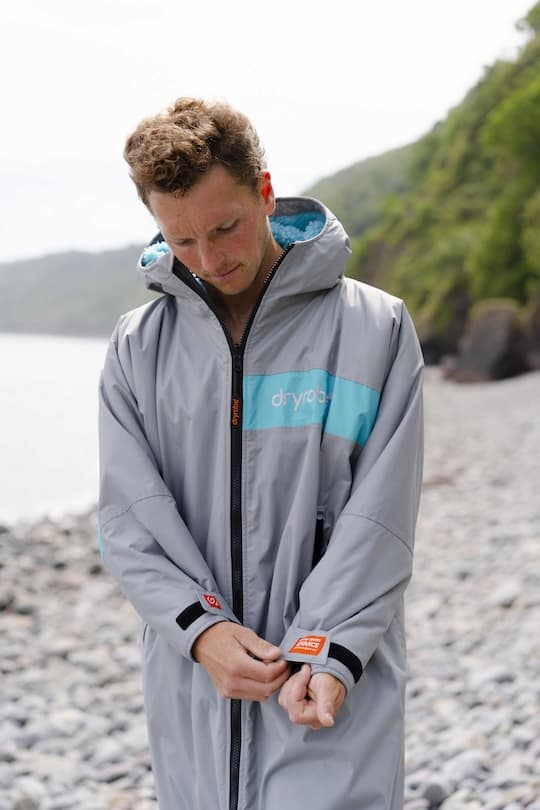 Man wearing a Dryrobe® while pulling his sleeve with a coastal scene in the background