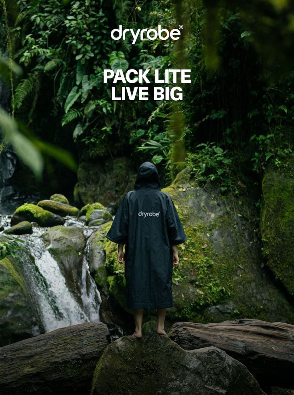 Person wearing a Dryrobe® Lite in the jungle while looking up at a waterfall