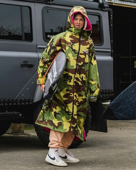 Lila Skinner in a dryrobe® carrying a surfboard