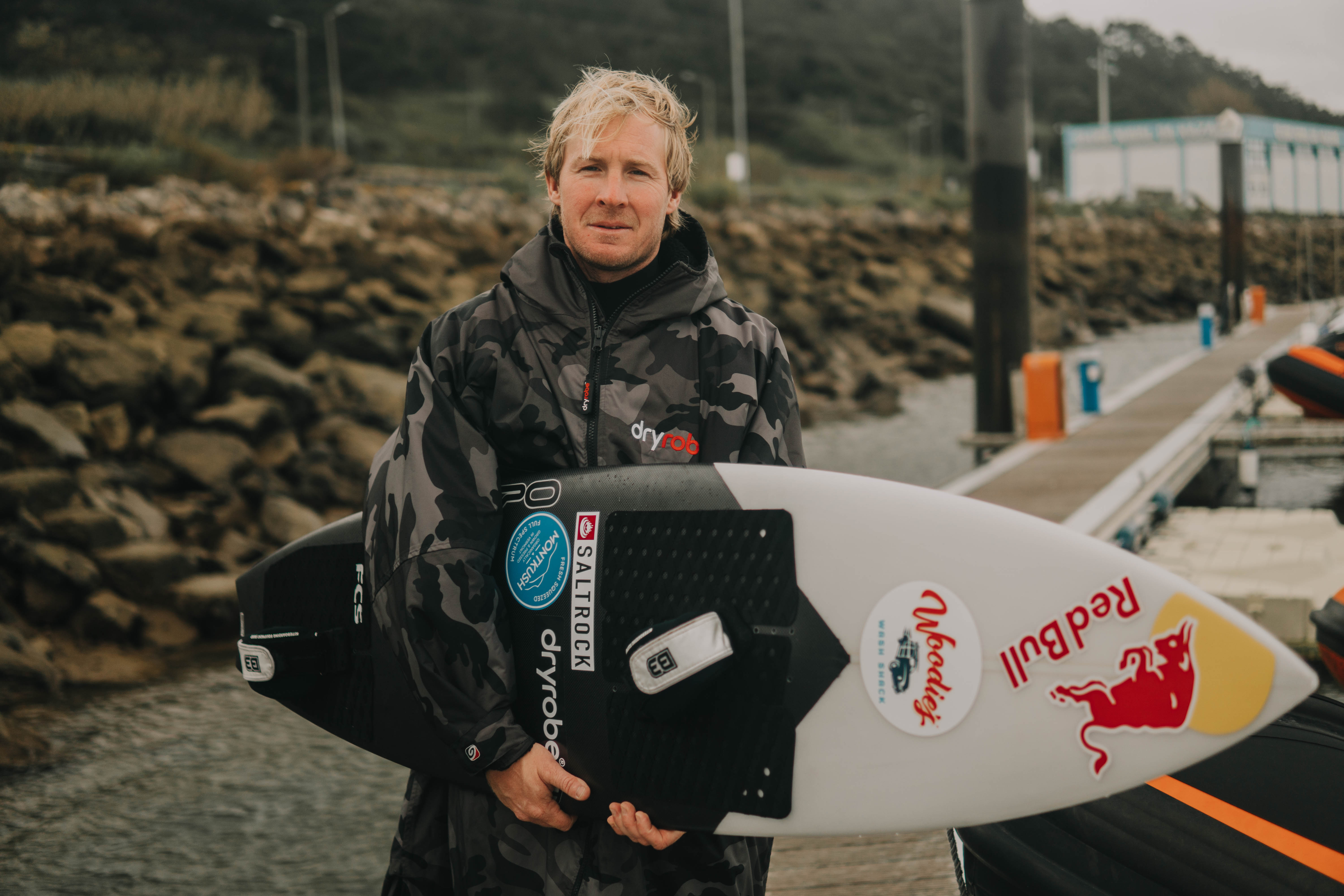 Andrew Cotton holding a surf board whilst wearing a dryrobe Advance changing robe
