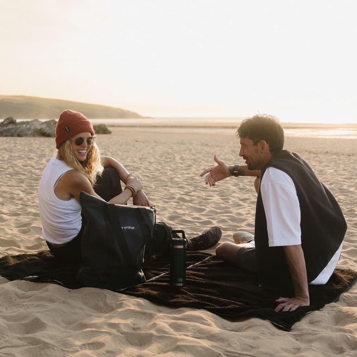Couple on the beach at sunset sitting on a Dryrobe® REWORK Large Picnic Blanket