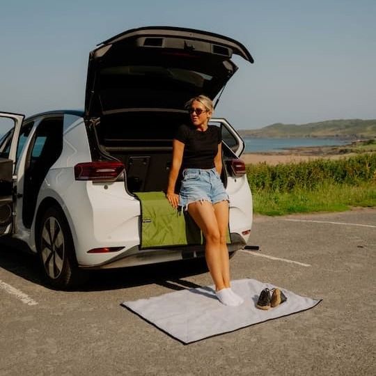 Woman using Dryrobe® REWORK Utility Mat by the car beside the beach