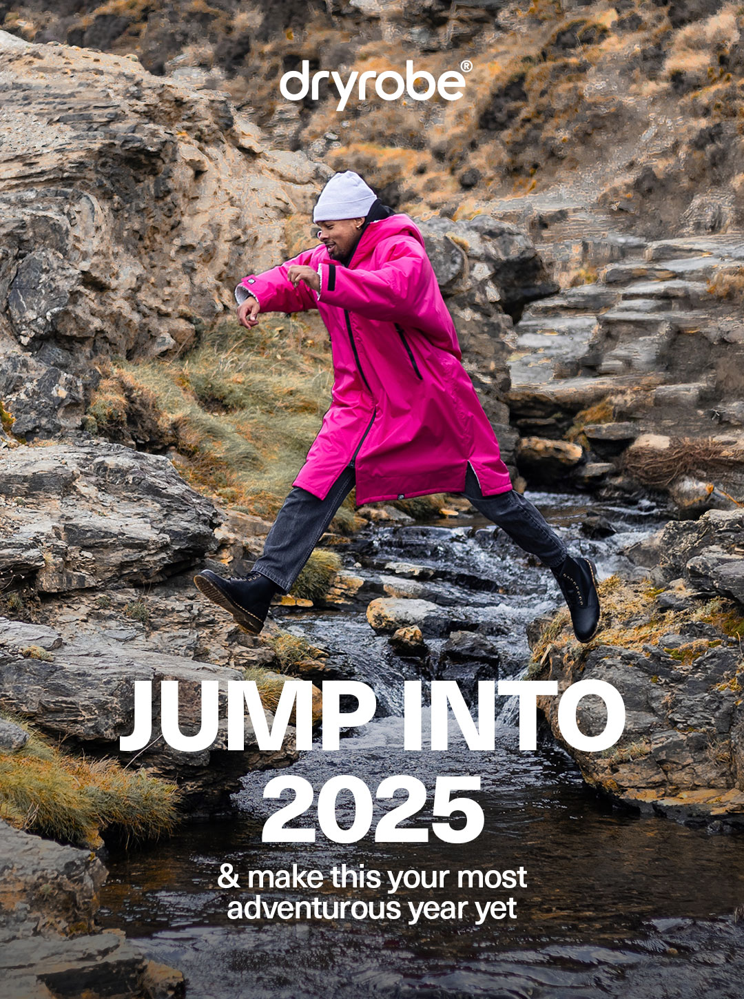 Man jumping over a stream while wearing a pink dryrobe® Advance