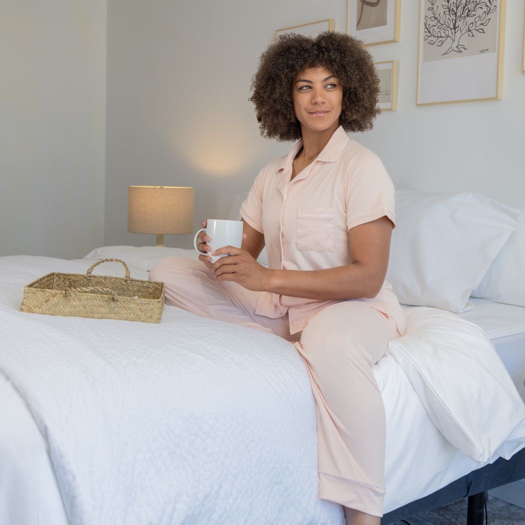 A woman sits on her bed with a cup of coffee