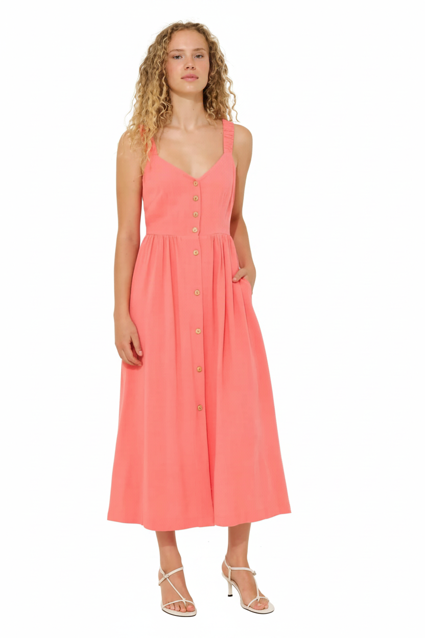 A woman in a coral button-front midi dress and white strappy heels stands against a white background.