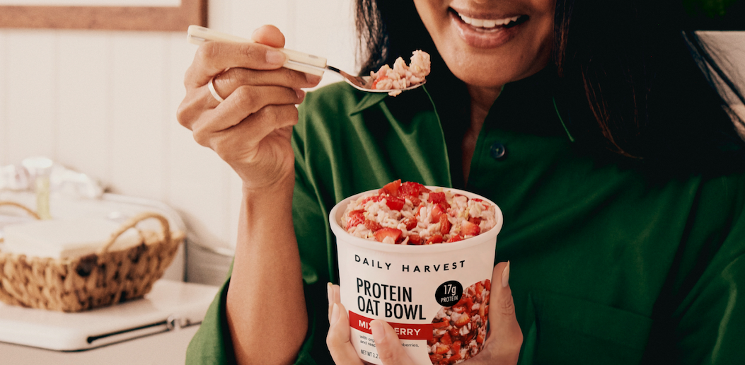 Close-up of a Daily Harvest protein oat bowl in mixed berry flavor, shown with a spoon taking a bite.