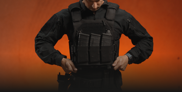 Tactical operator in black uniform adjusting black plate carrier with magazine pouches