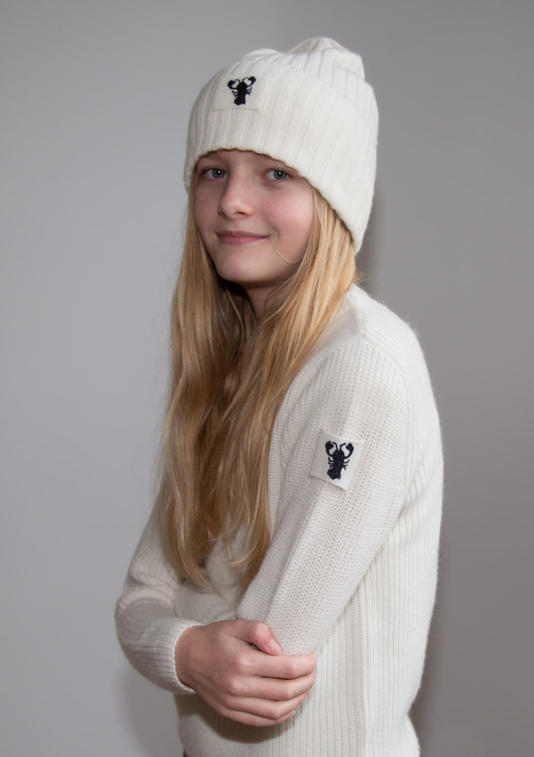 Porträt Mädchen in weissem Kaschmirpullover JENSON und mit weisser Mütze – beides mit Lobster-Emblem