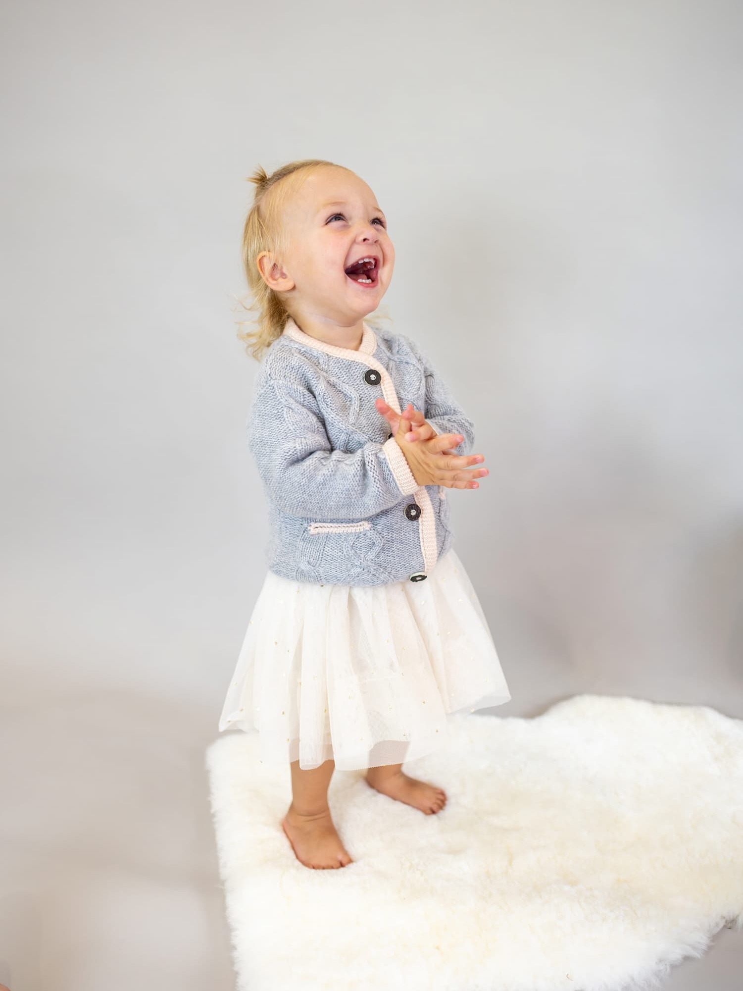 Toddler Mädchen in Kaschmirjacke MAXI und Röckchen schaut lachend nach oben.