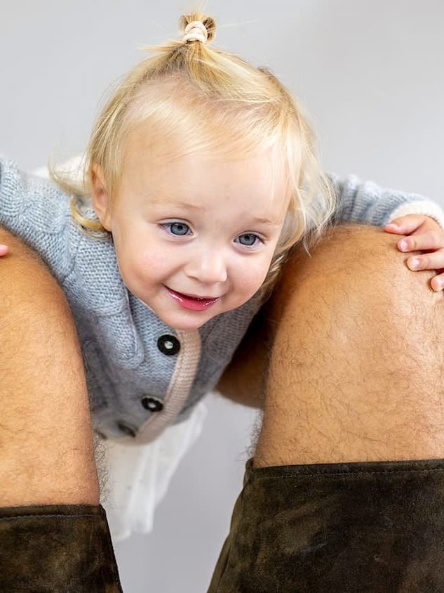 Toddler Mädchen in Kaschmirjacke MAXI lugt durch die Beine vom Papa