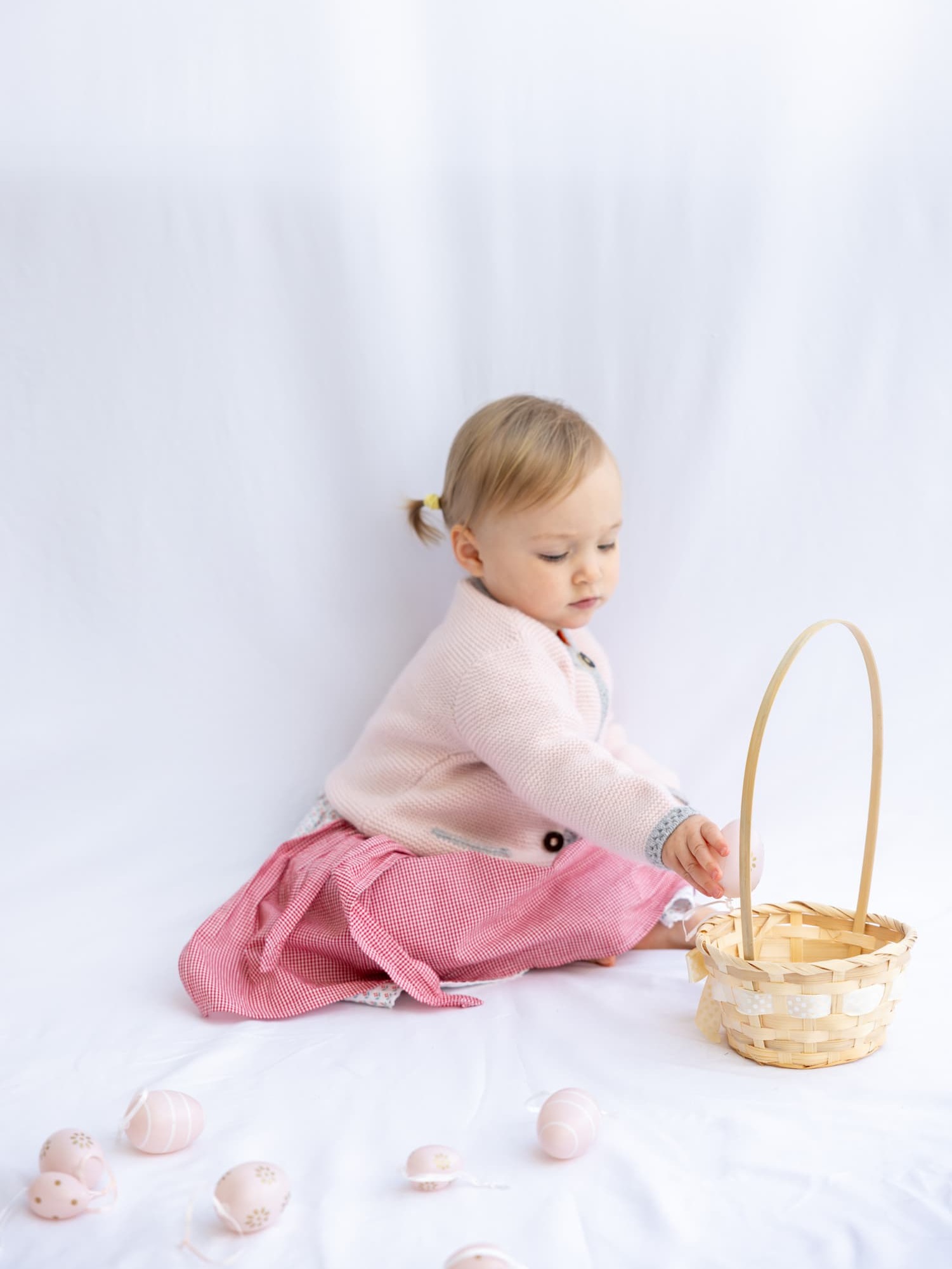 Sitzendes Babymädchen mit Kaschmir-Trachtenjacke und Osterkorb