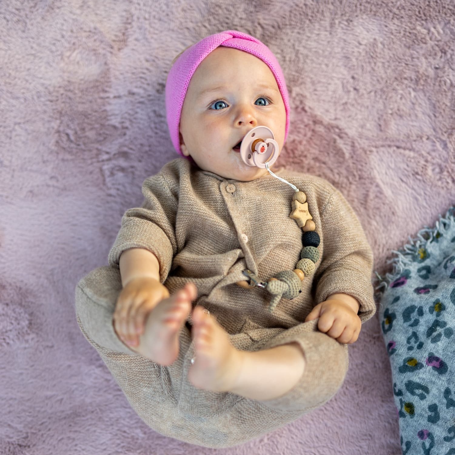 Baby auf Rücken liegend in Kaschmir-Overall ANOUK in Beige mit Stirnband MAXI in Rosa
