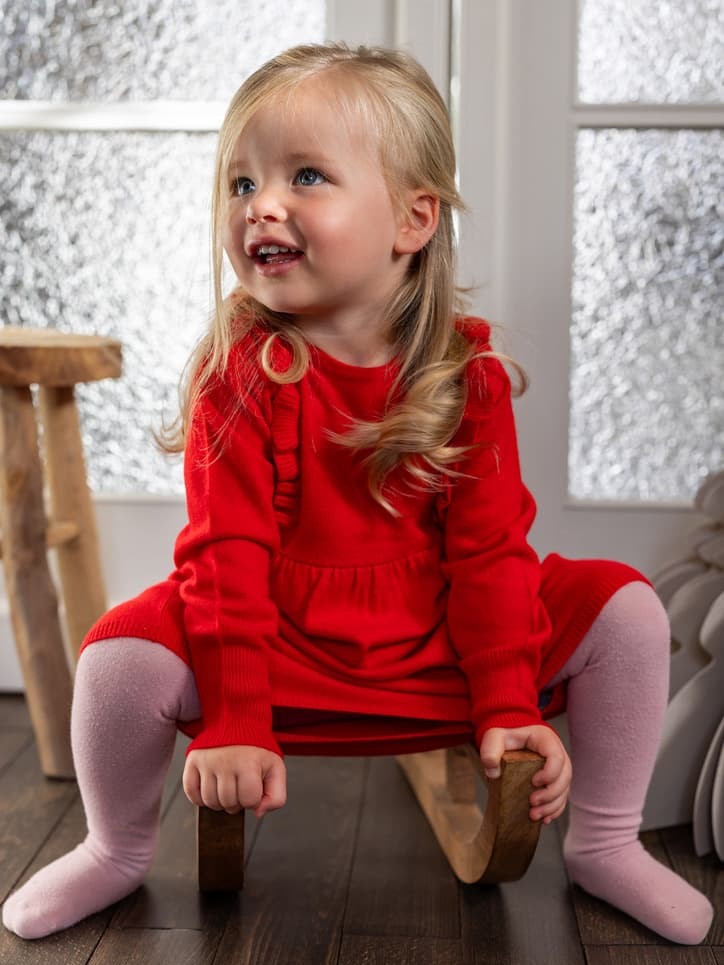 Kleines Mädchen in rotem Kleid auf Schlitten