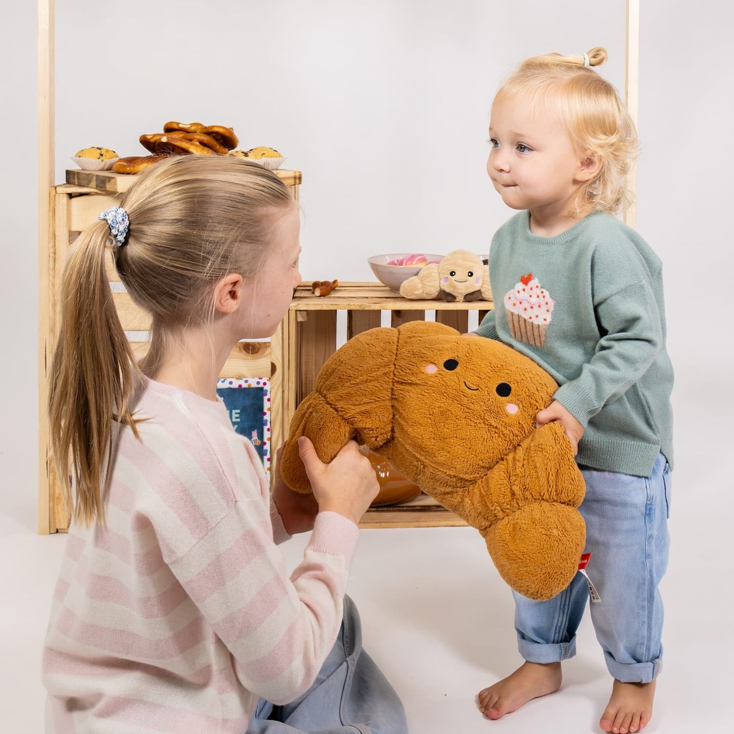 Zwei Mädchen in Kaschmirpullovern spielen in gebasteltem Bakery-Setting