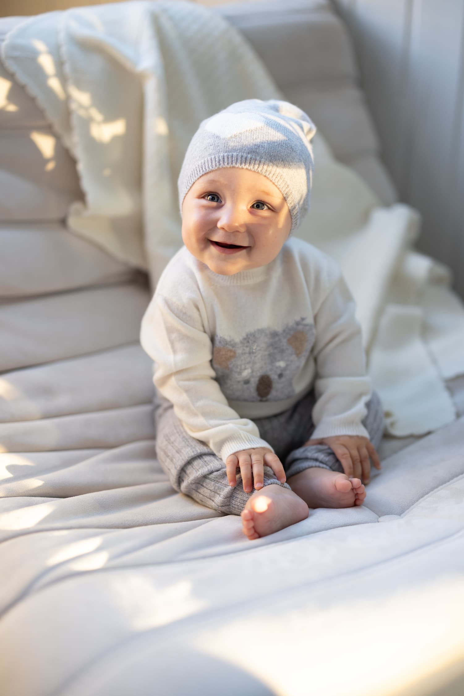 Baby sitzend auf Sofa mit Kaschmir Pullover KOALA, hellgrauer Kaschmirmütze und -Leggings